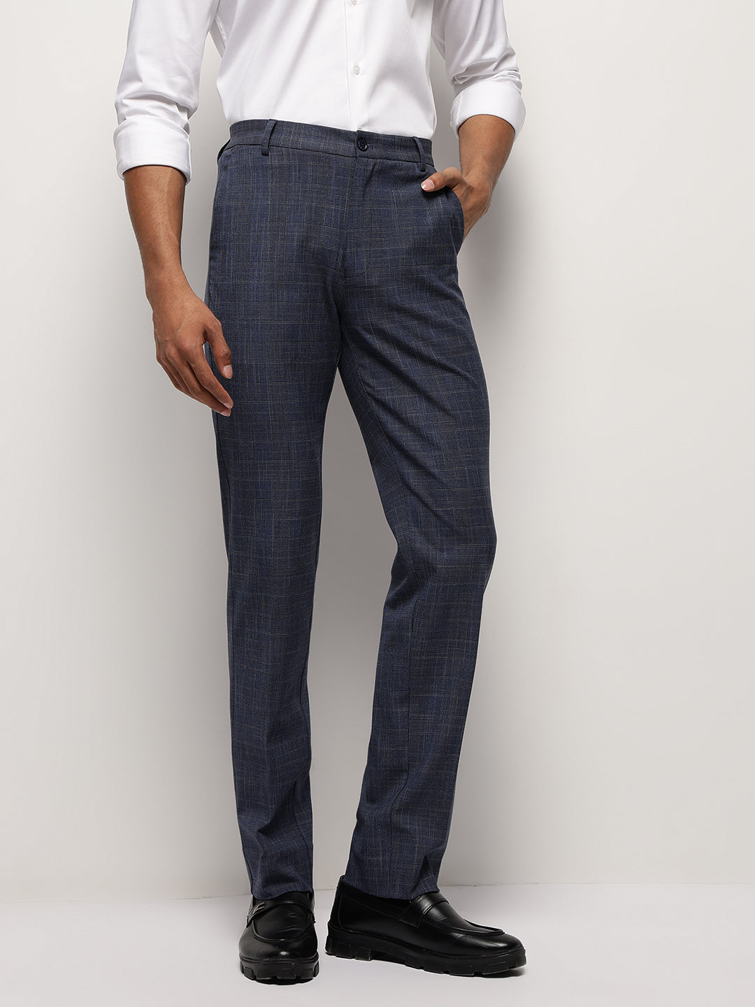 A man standing against a white background, wearing steel blue, slim-fit, formal trousers with a flexible waistband, flat front, button and zip, made of stretch fabric.