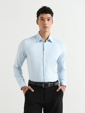 A man wearing a light blue long-sleeve dress shirt, black trousers, and a black belt, standing against a plain white studio background.