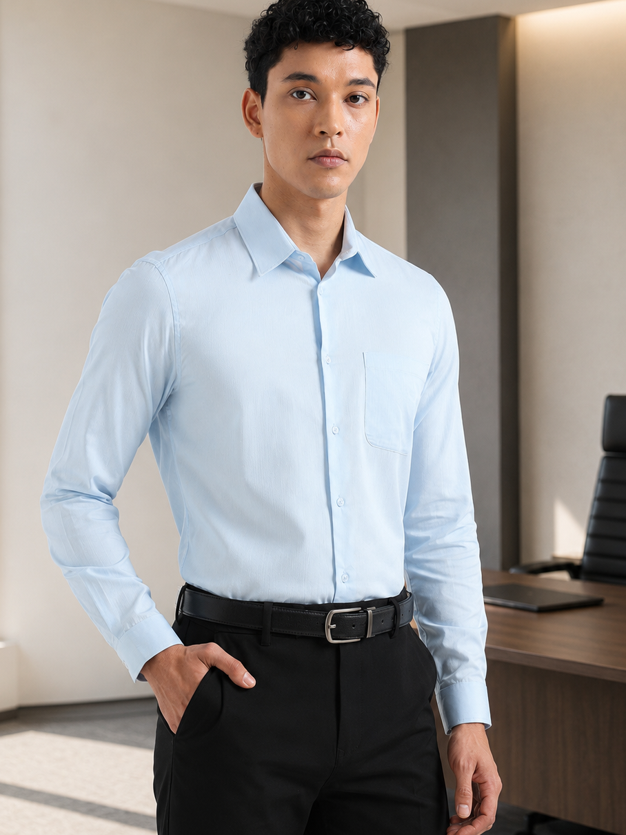 A man wearing a light blue long-sleeve button-down dress shirt, black trousers, and a black belt, standing in a modern office environment.